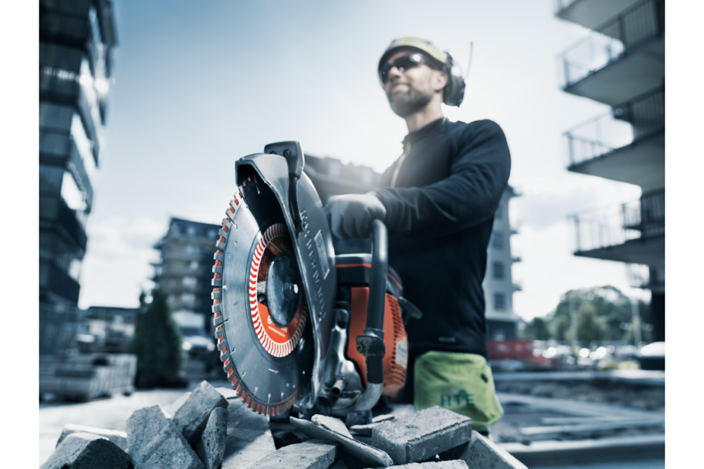 Operator in safety gear holding a Husqvarna K 770 beside stacked kerbs and paving blocks