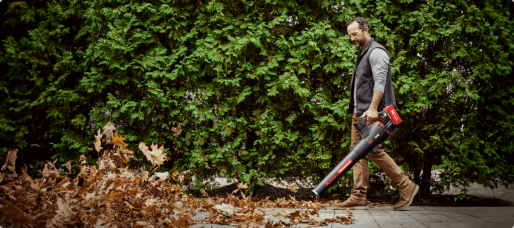 Operator clearing leaves along a hedge with a Kress KC510 60 V handheld blower