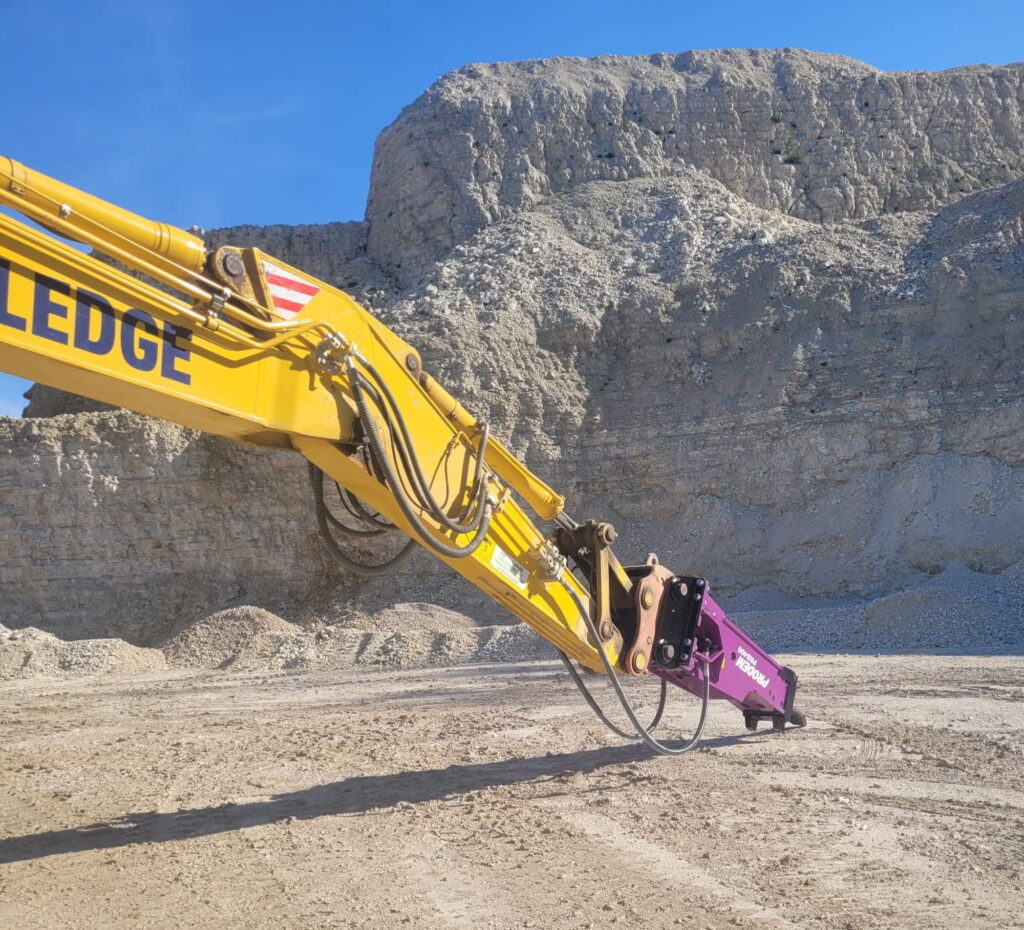ProDem hydraulic hammer on the arm of a yellow excavator in a quarry