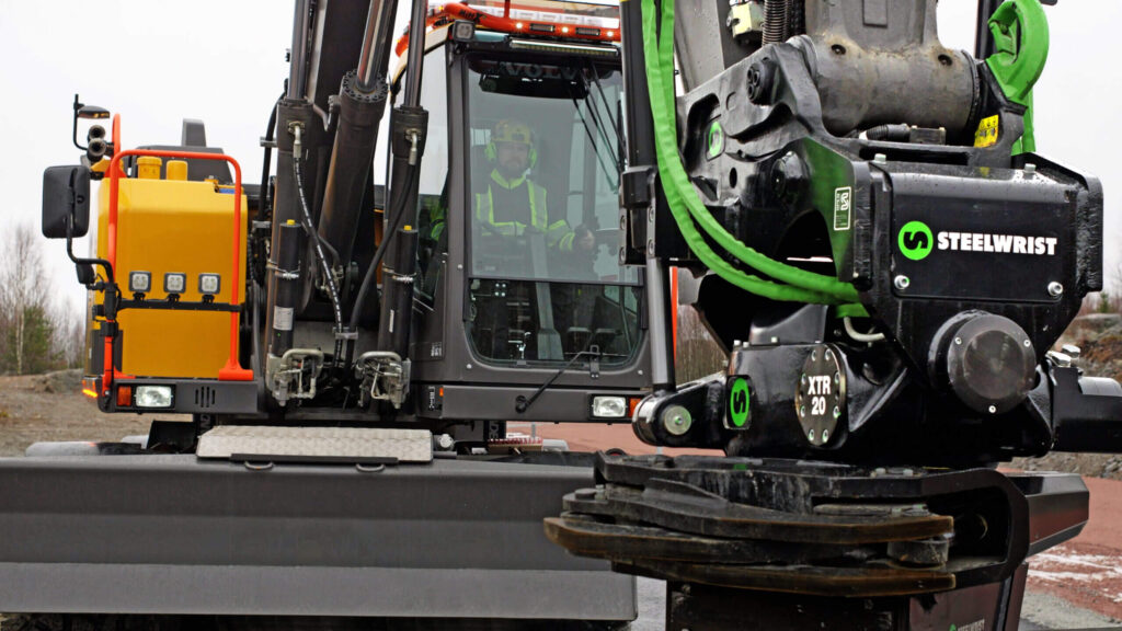 Close-up of a Steelwrist XTR20 tiltrotator on an excavator with the operator in the cab behind